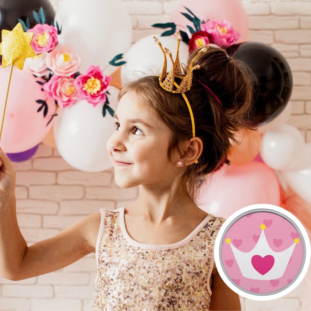 Meisje met toverstaf, kroontje op, glimlachend met ballonnen en bloemen op de achtergrond.