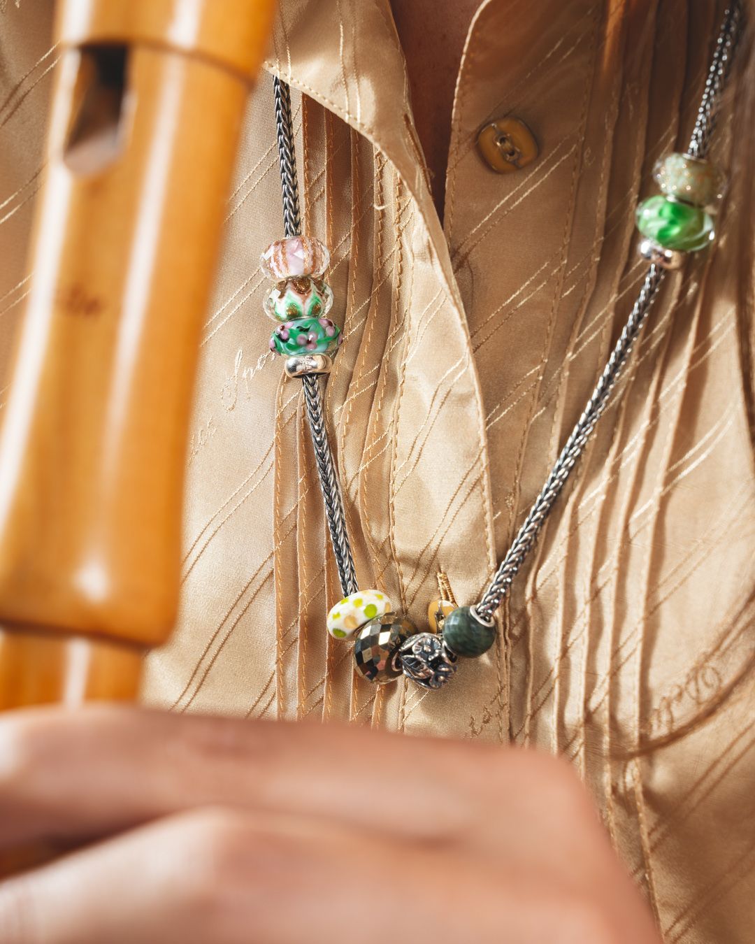 Close-up van een persoon die een fluit vasthoudt en een ketting met kleurrijke kralen draagt op een gouden shirt.