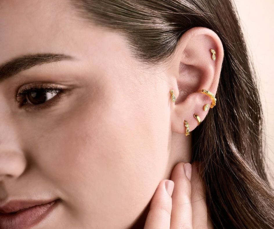 Vrouw met meerdere gouden oorbellen, die haar nek aanraakt.