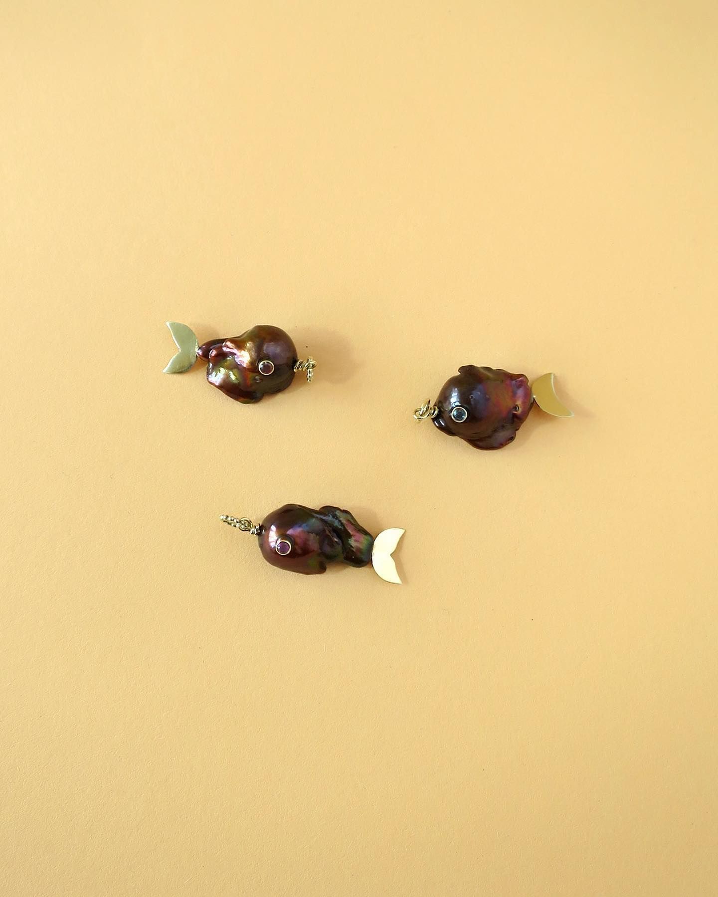 Drie bruine parelvissen met gouden vinnen op een gele achtergrond.