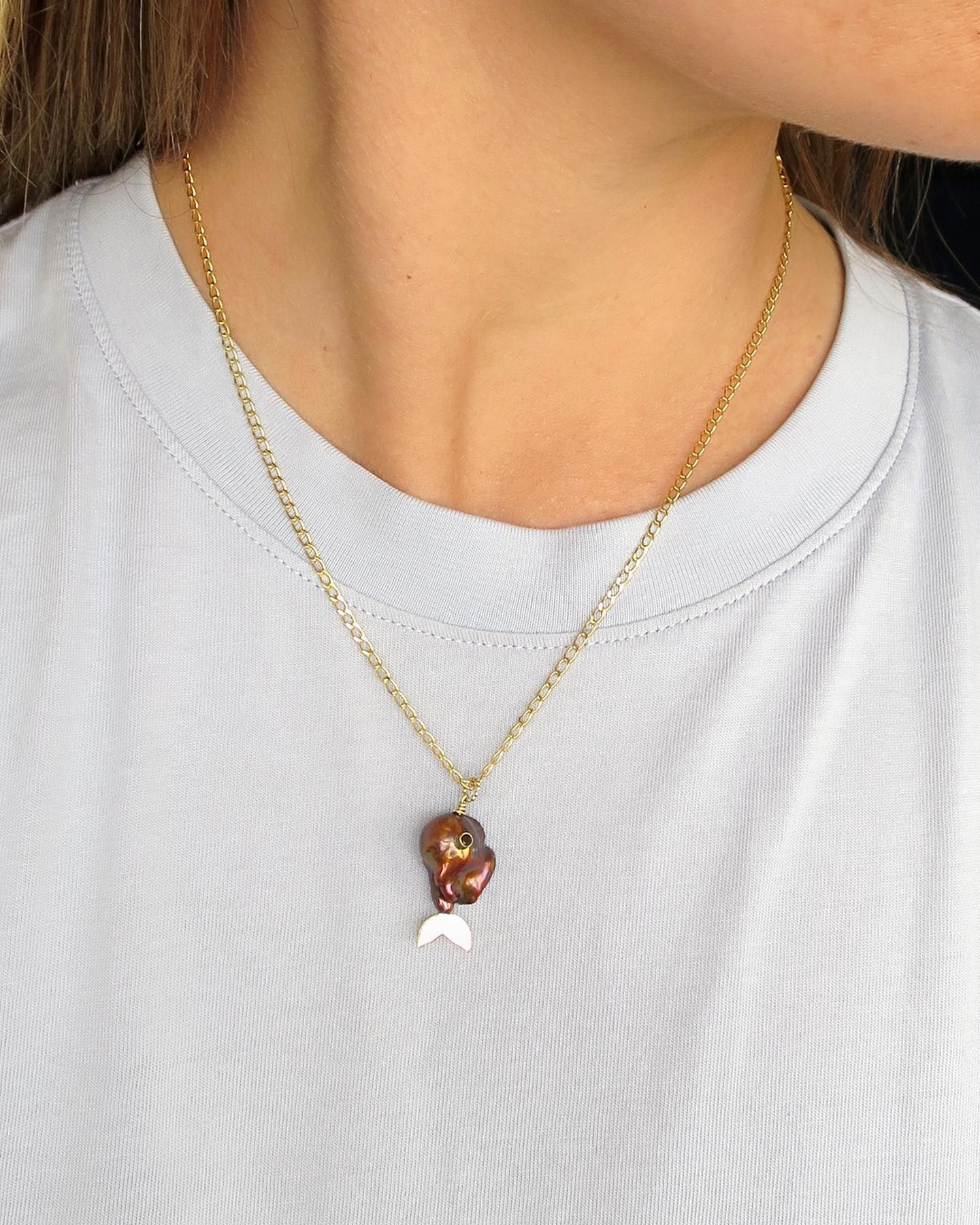 Vrouw draagt een gouden ketting met een bruine hanger en een zilveren halve maan.