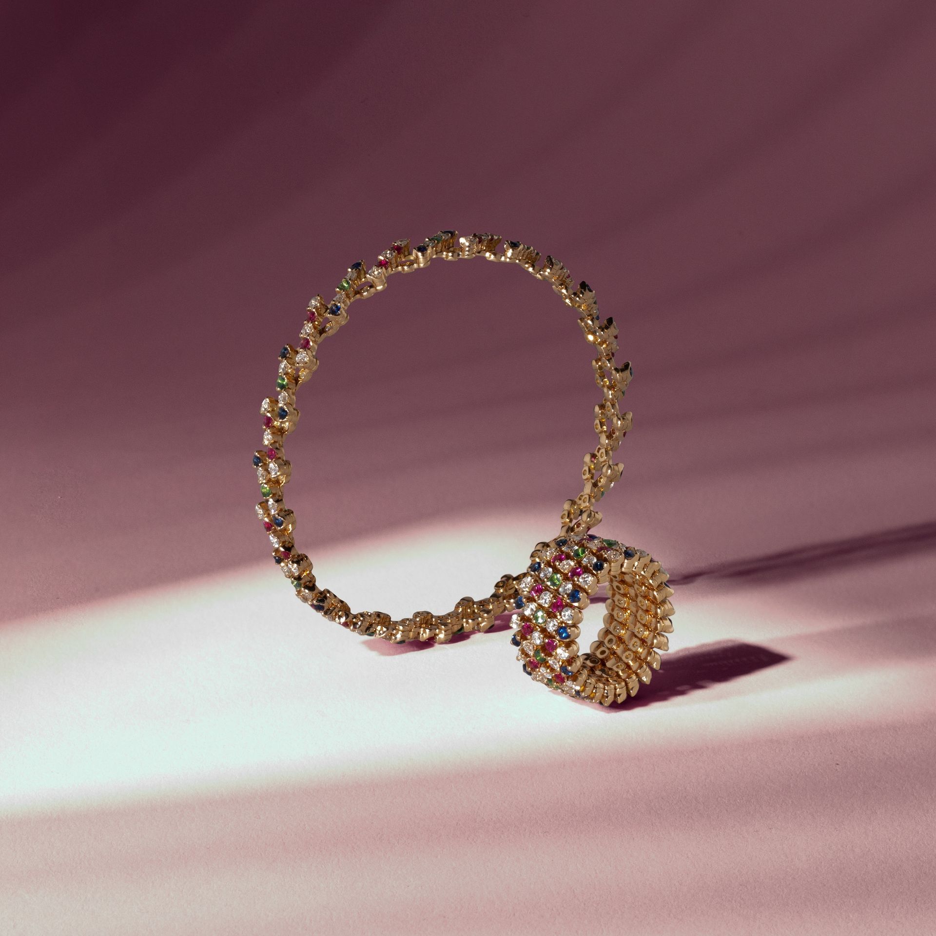 Gouden ketting met kleurrijke edelstenen, op roze achtergrond.