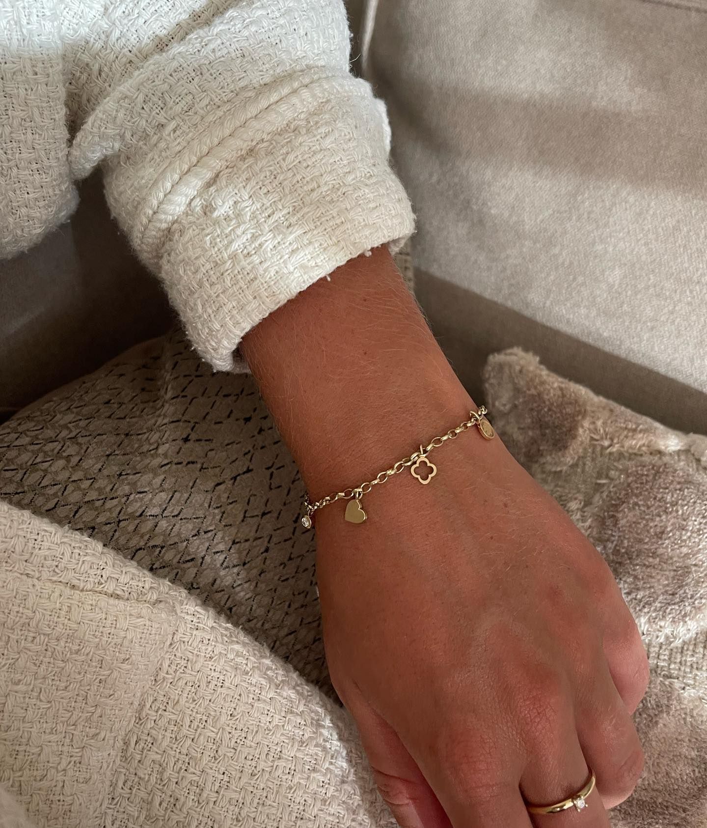 Gouden bedelarmband voor om de pols, met crèmekleurige trui-mouw.