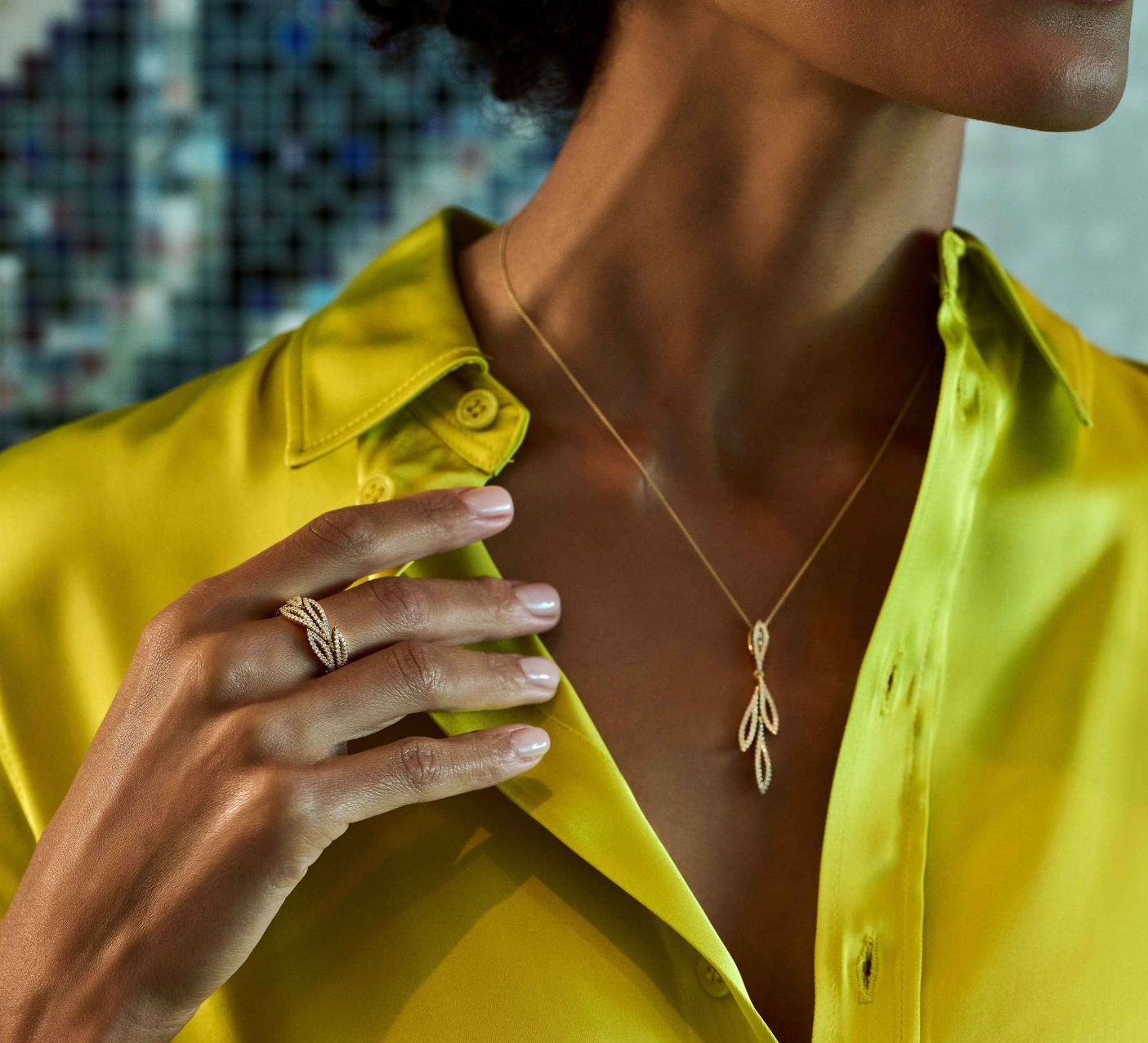 Vrouw draagt gouden sieraden, ring en hanger aan ketting, op gele zijden blouse.