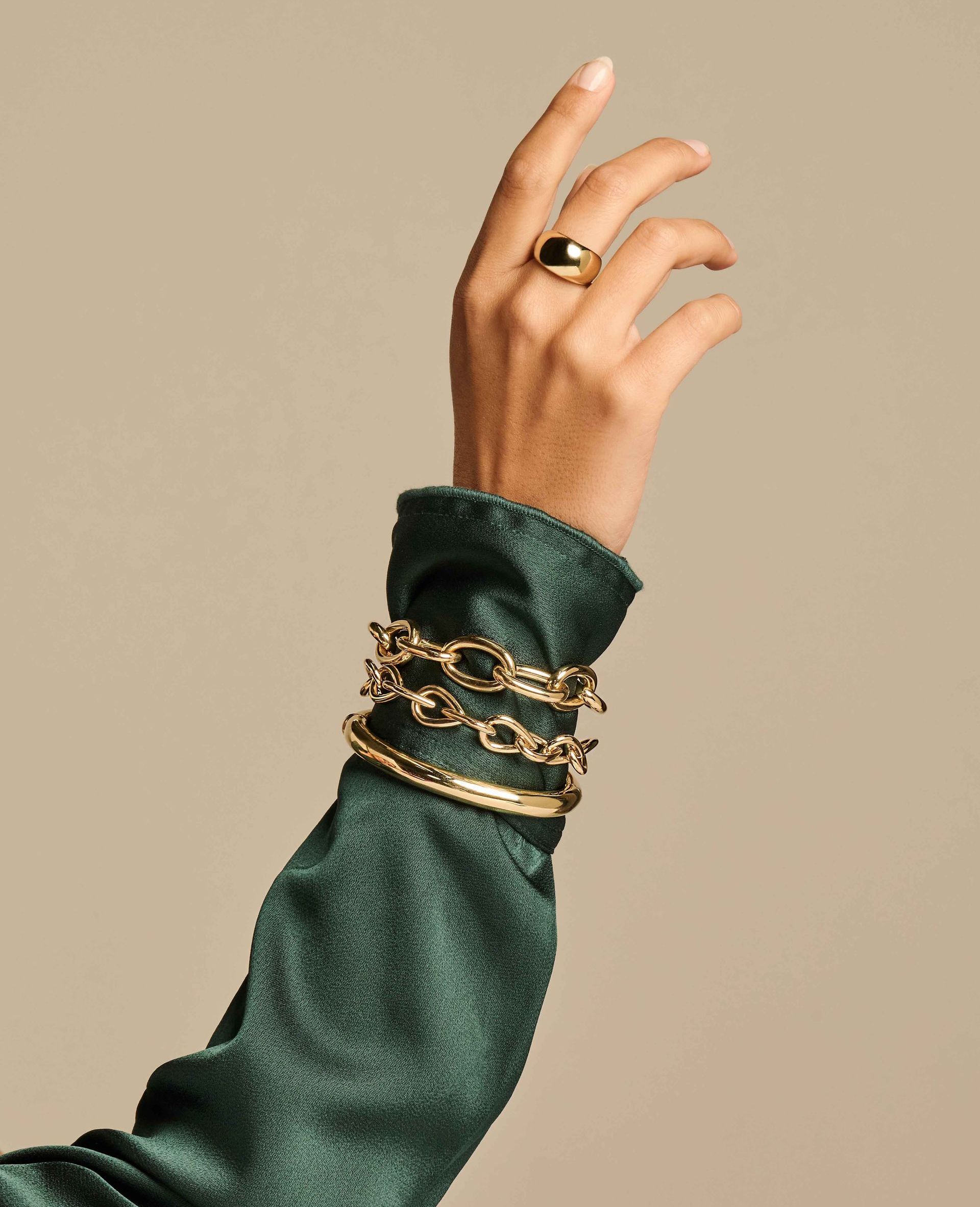 Hand met gouden sieraden, armbanden en ring, mouw van groen topje.