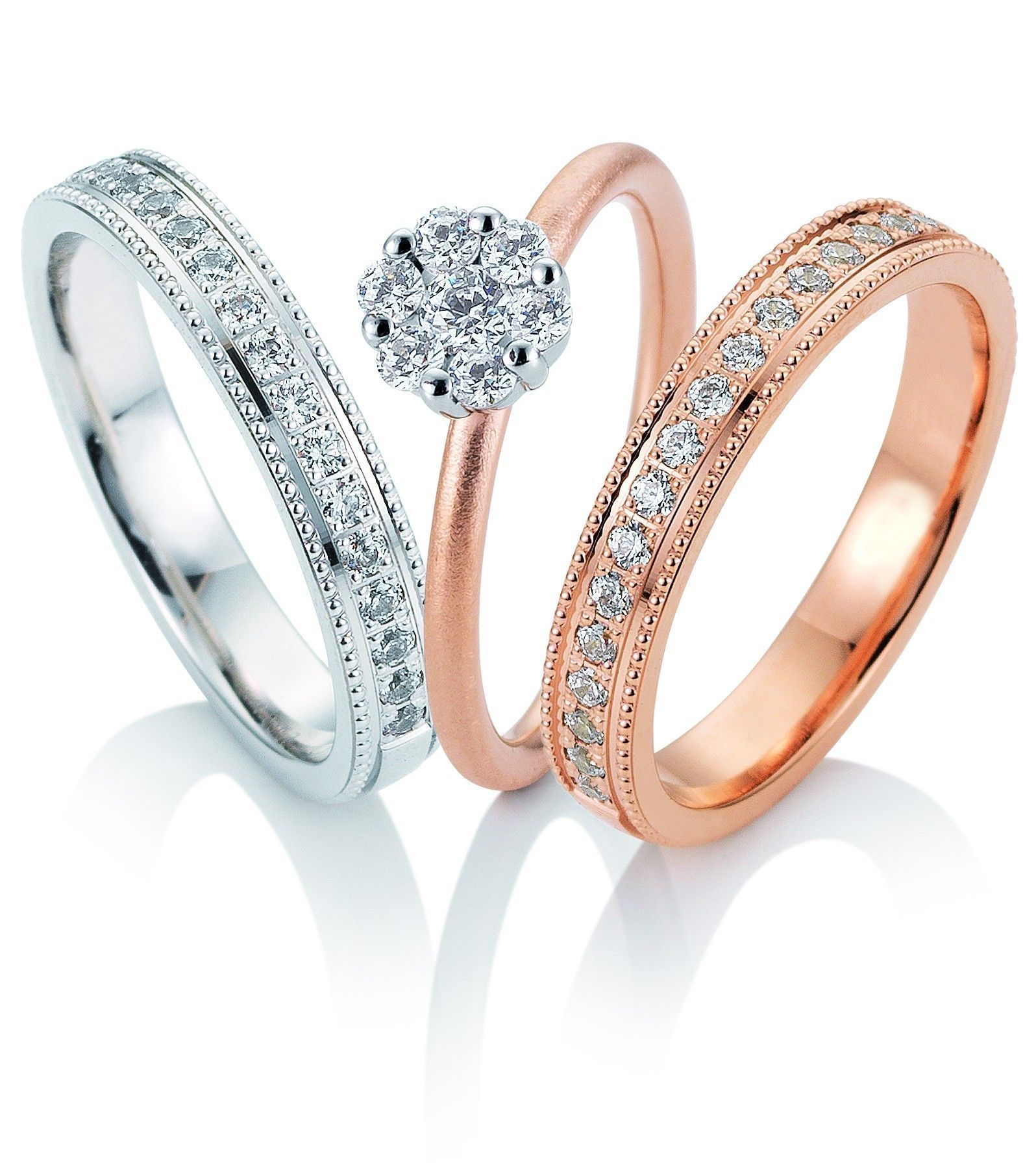 Drie ringen met diamanten: een band van witgoud, een clusterring met diamanten, een band van roségoud, op wit.