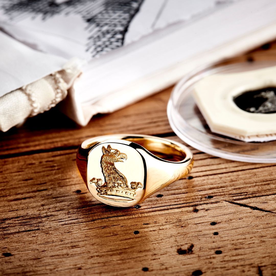 Gouden zegelring met gegraveerd dierenembleem op een houten oppervlak.