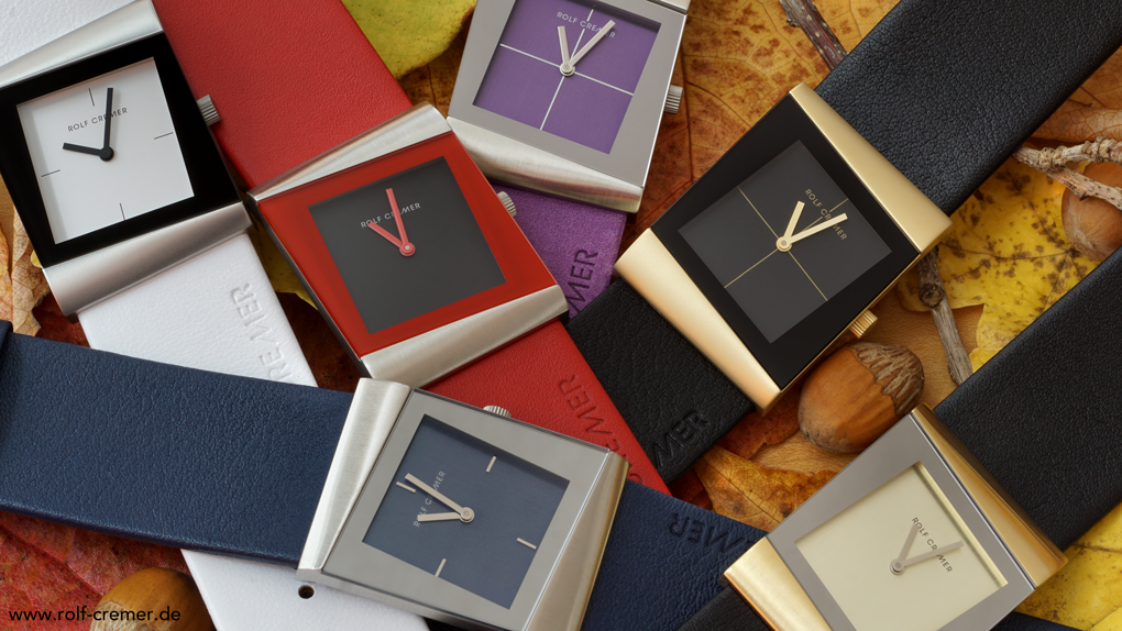 Close-up van verschillende kleurrijke horloges met vierkante wijzerplaten, liggend tussen herfstbladeren.