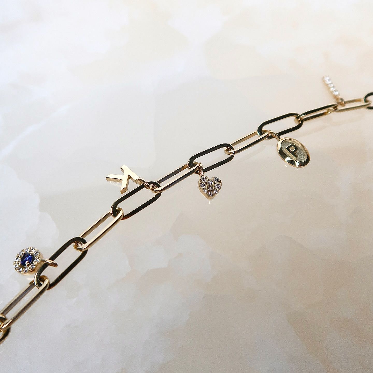 Gouden bedelarmband met diverse bedels, waaronder een letter 