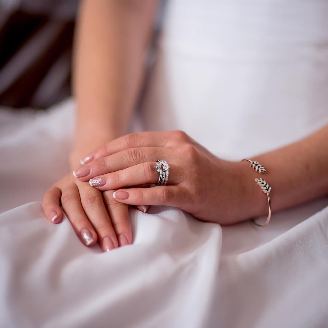 Close-up van een hand met een ring en een armband rustend op een witte stof.