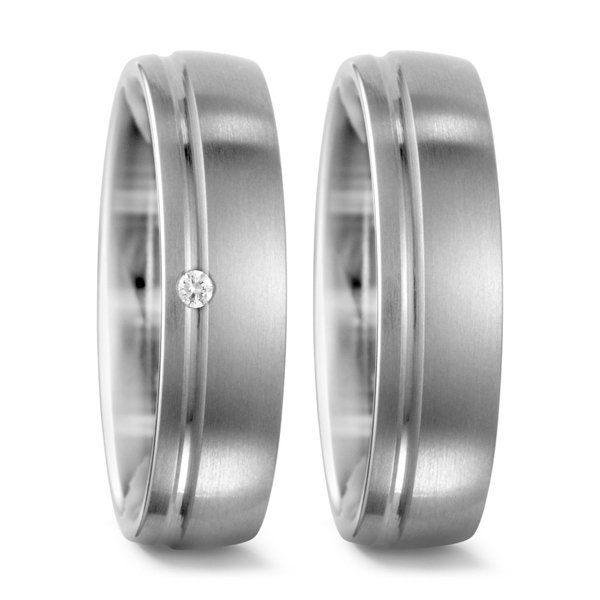 Twee zilveren trouwringen, waarvan één met een klein diamantje, tegen een witte achtergrond.