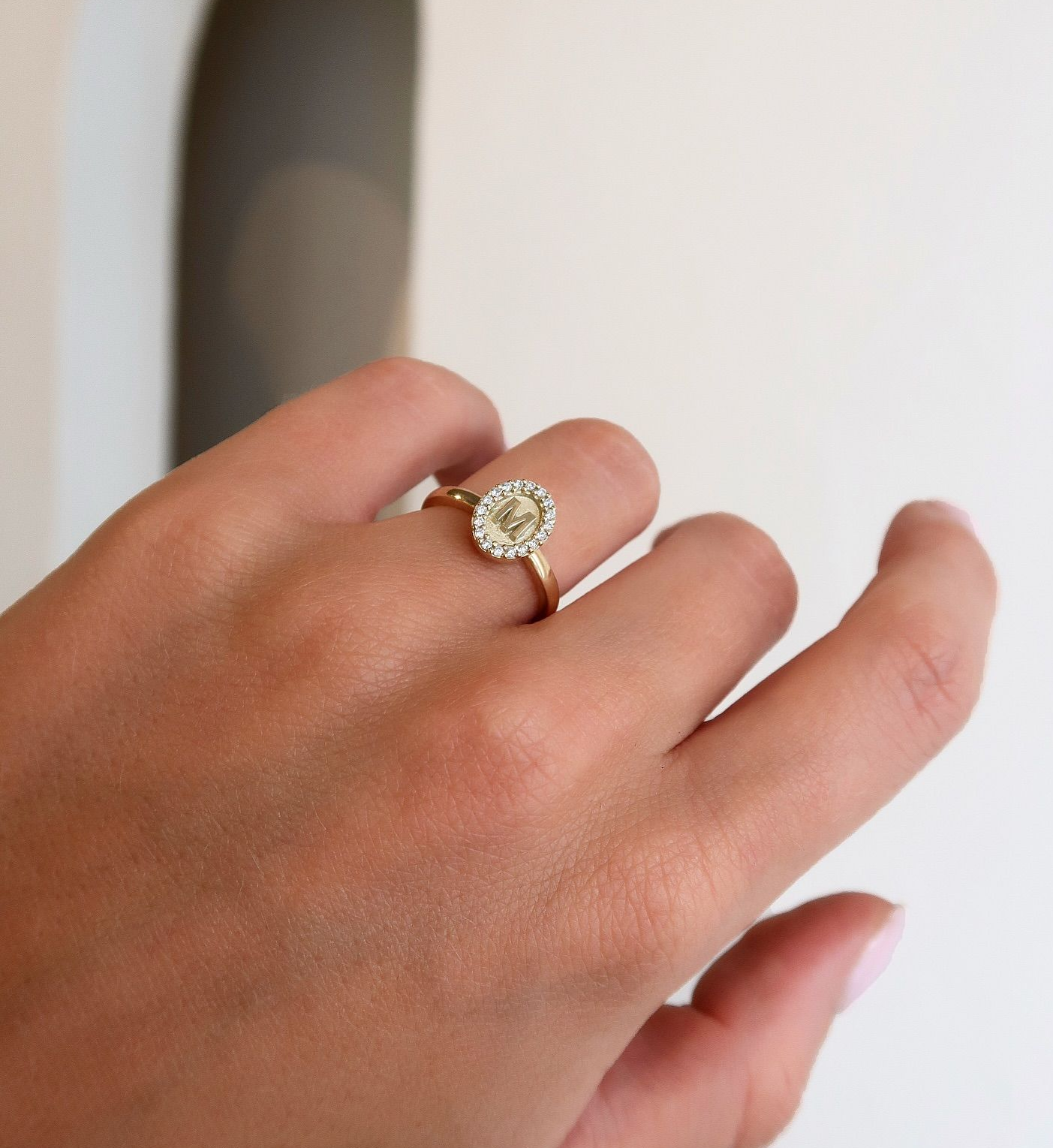 Hand met een gouden ring met een ovale steen in het midden en een halo van kleinere stenen.