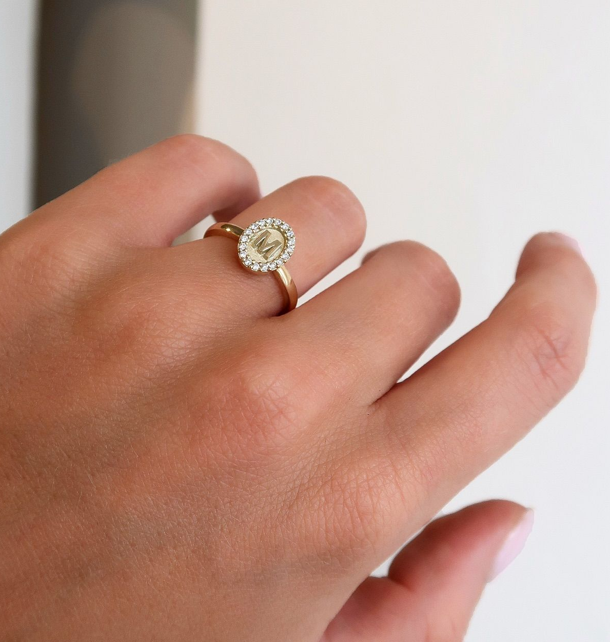 Aan de hand van de vrouw draagt ​​ze een gouden ring met een ovaal geslepen centrale steen, bezet met een halo, en kleinere stenen eromheen.