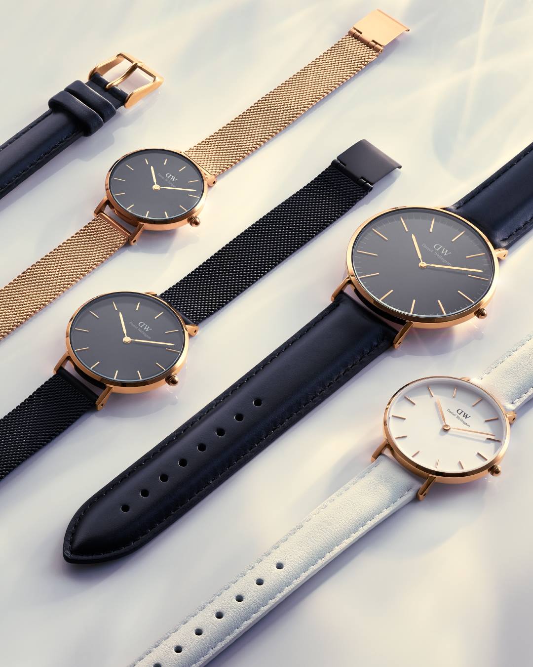 Vijf polshorloges met gouden kasten en verschillend gekleurde bandjes op een wit oppervlak.