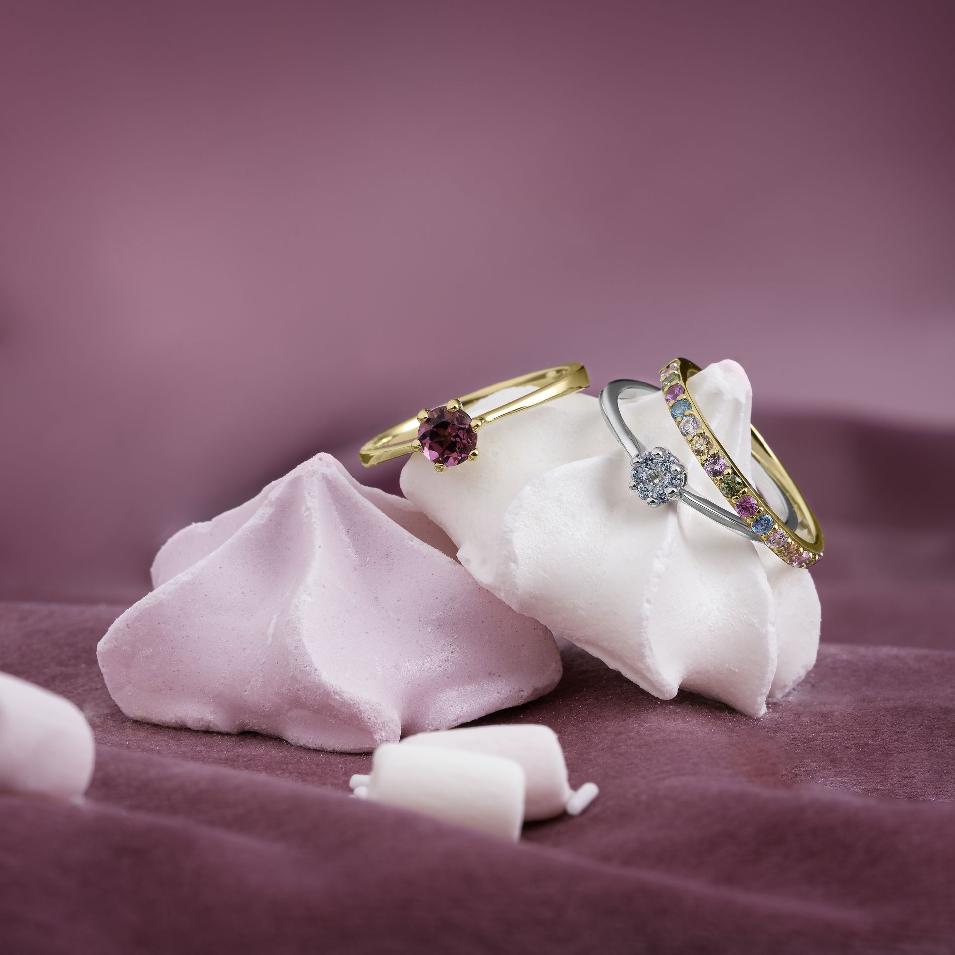Ringen met edelstenen op meringue. Goud, zilver en kleurrijke edelstenen, gezet op roze stof.