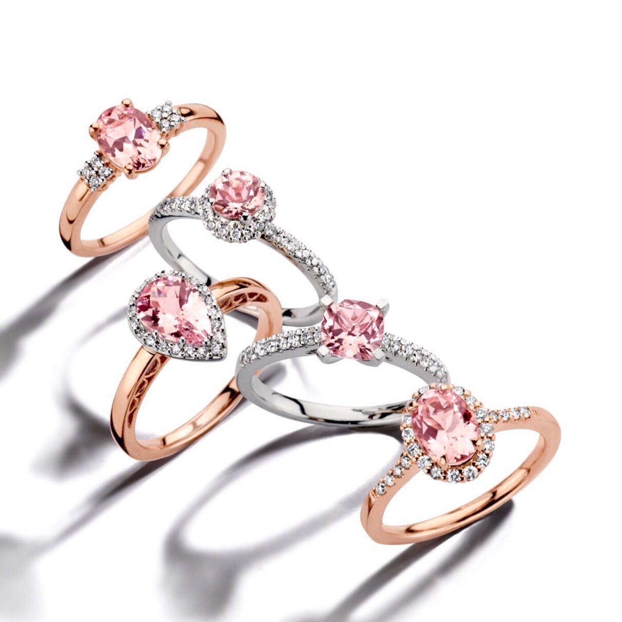 Vijf ringen met roze edelstenen en diamanten accenten op een witte achtergrond.