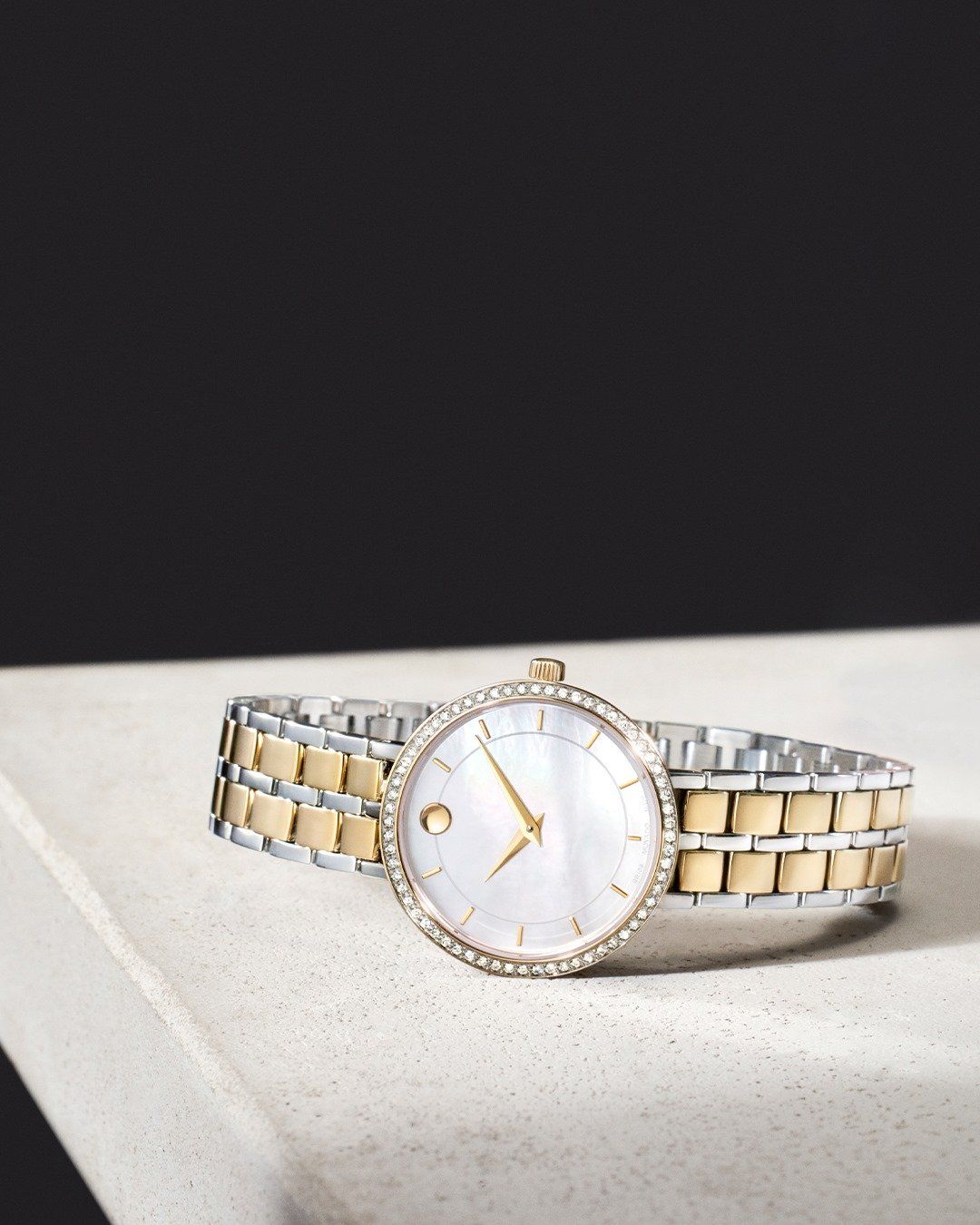 Zilveren en gouden polshorloge met een parelmoeren wijzerplaat en diamanten lunette op een wit oppervlak.