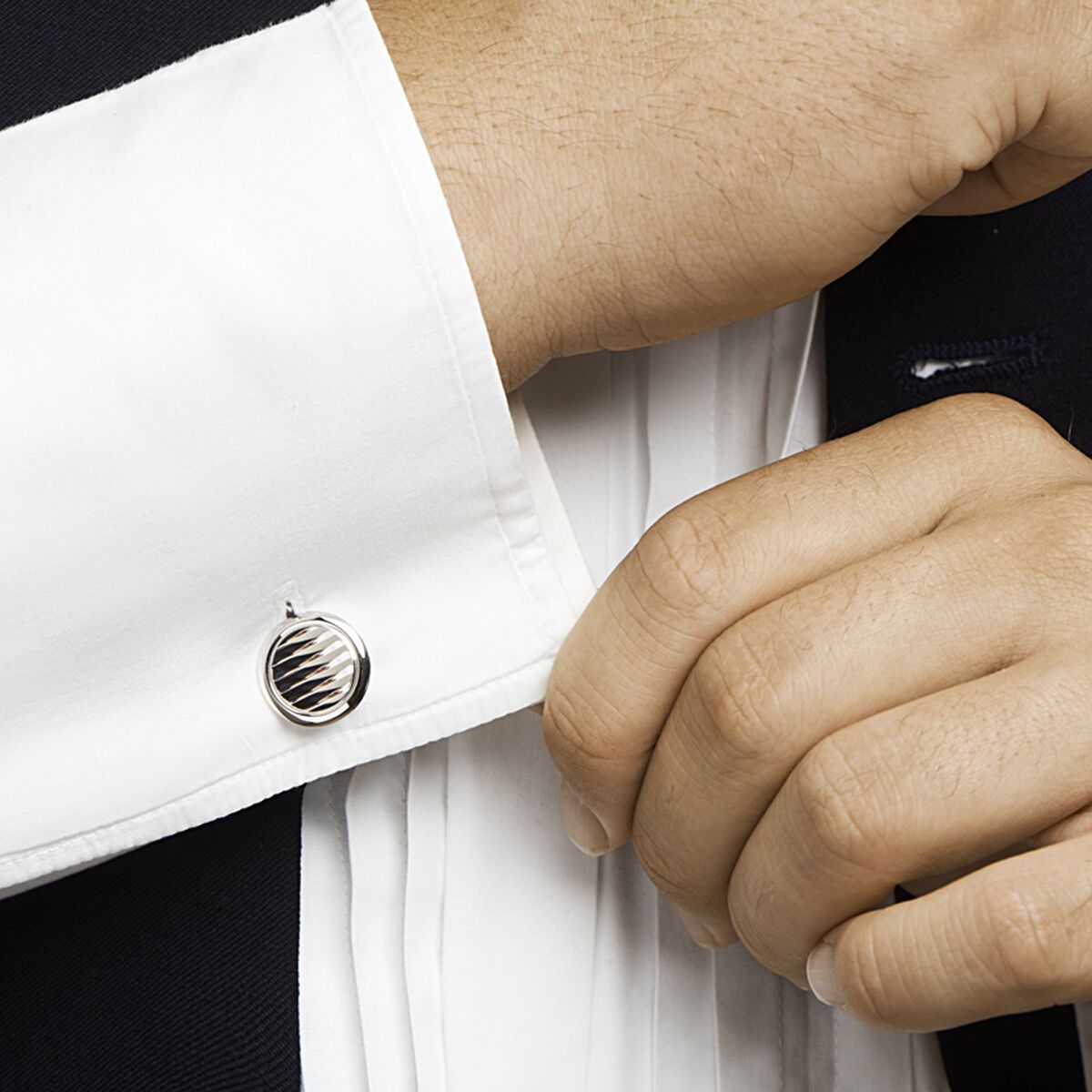 Een man die een manchetknoop op een wit overhemd verstelt, in een contrast met een donker pak.