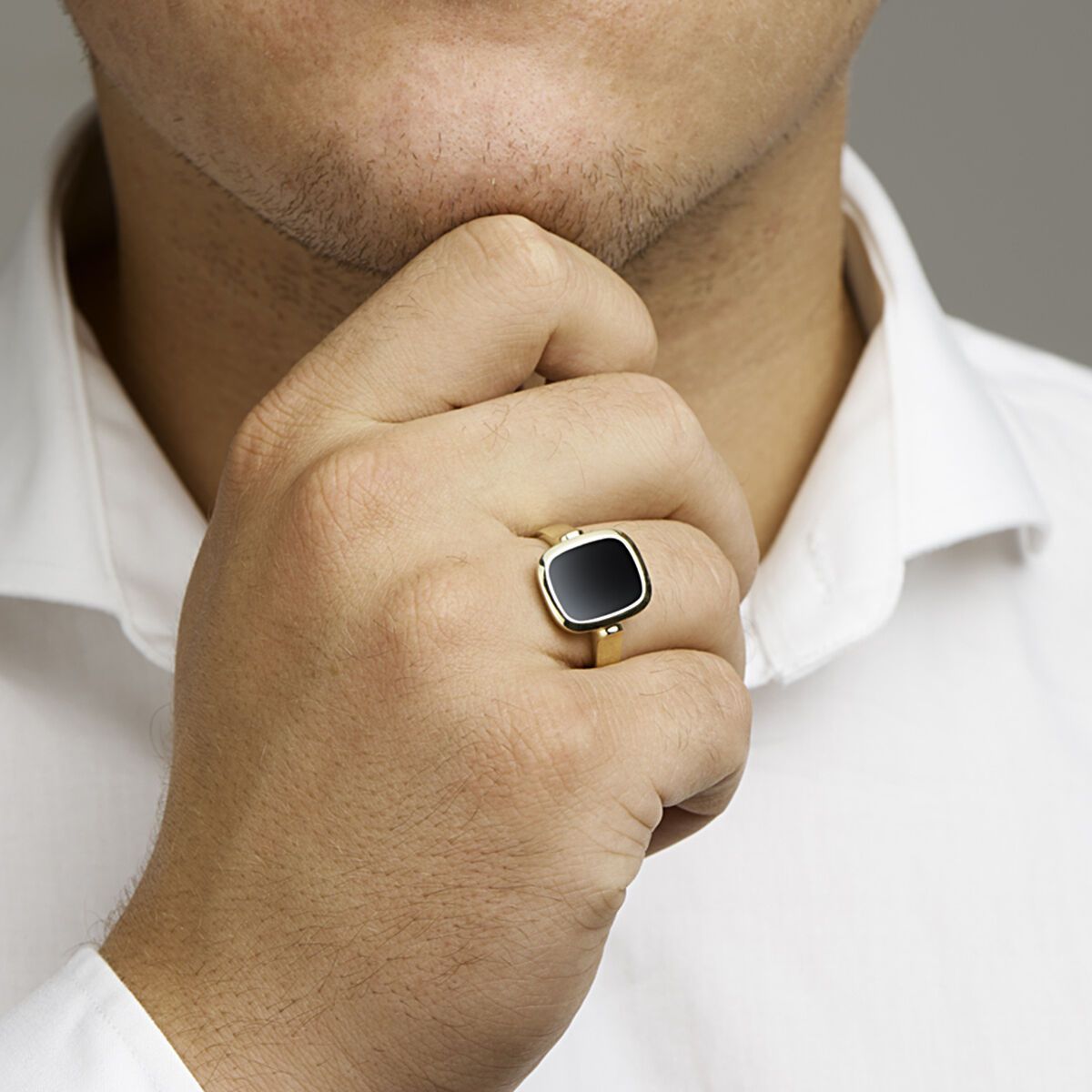 Man met een gouden ring met een zwarte vierkante edelsteen, zijn kin in zijn hand, gekleed in een wit overhemd.