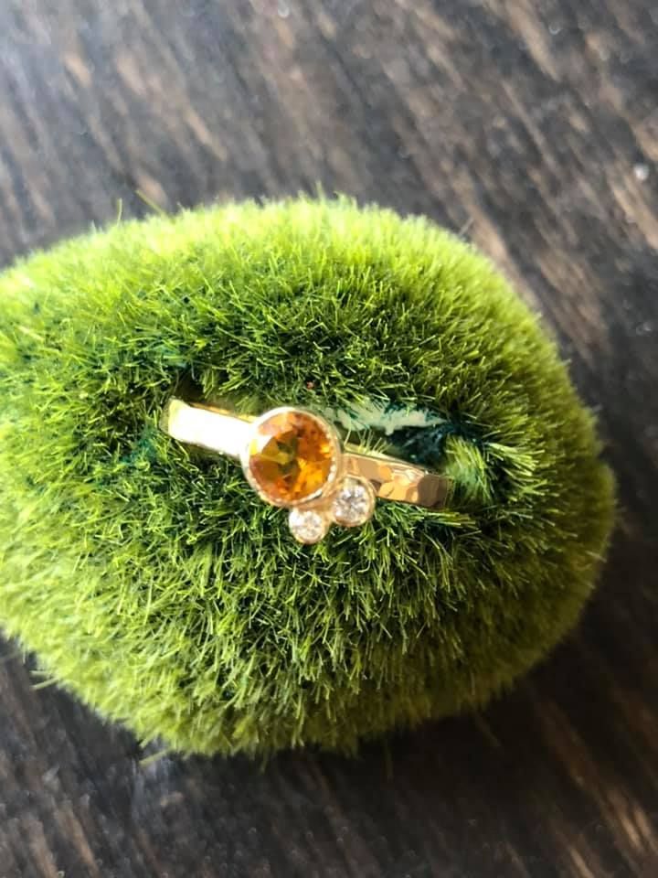 Gouden ring met oranje en witte edelstenen op een groen, met mos bedekt oppervlak.