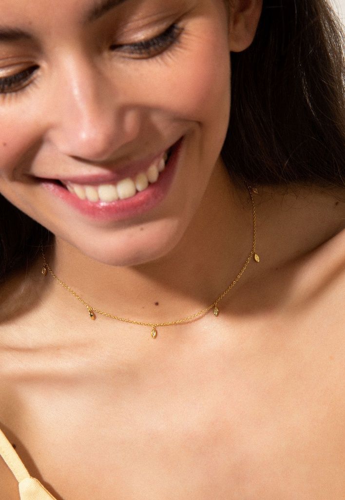 Lachende vrouw, die een gouden ketting draagt ​​met kleine bedeltjes.