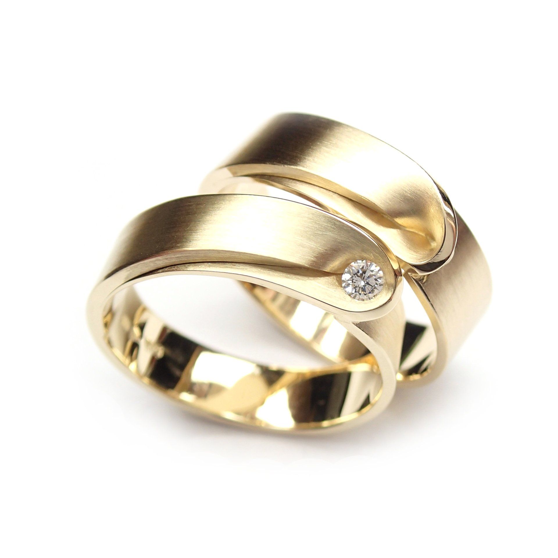 Twee overlappende gouden trouwringen, waarvan één met een klein diamantje.