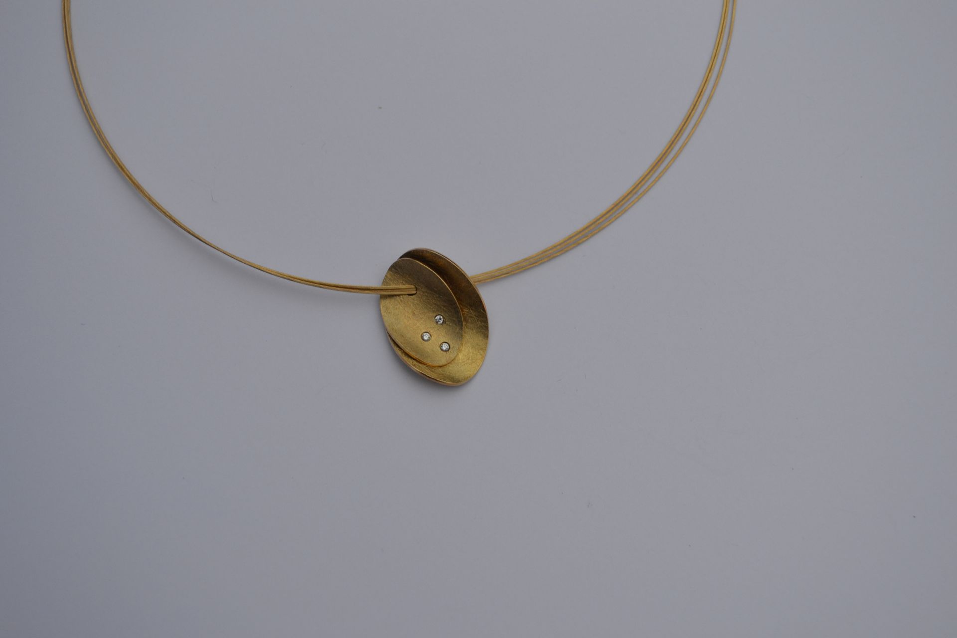 Gouden hangerketting met ovale bedel, twee kleine diamantjes en dunne gouden ketting.