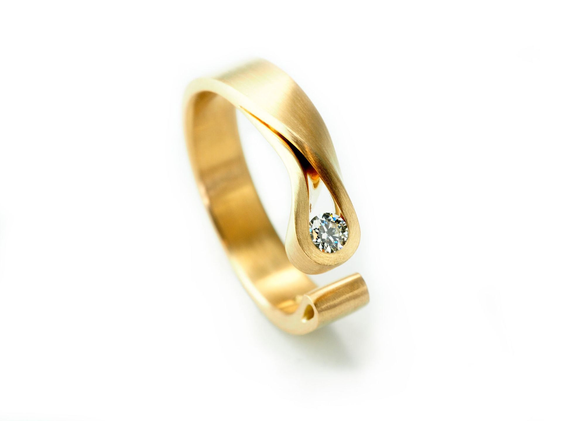 Gouden ring met ovaal vingerafdrukontwerp op een neutraal oppervlak, met een wazige witte achtergrond.