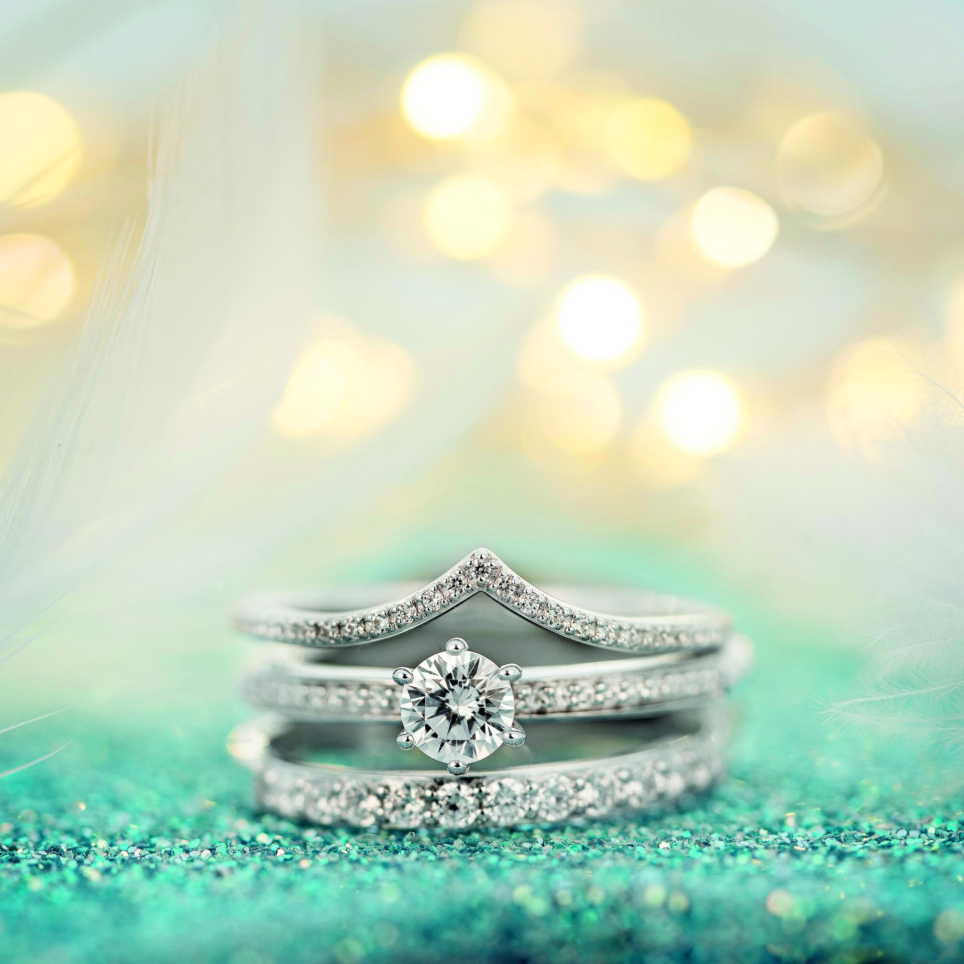 Een stapel diamanten ringen op een sprankelend turquoise oppervlak met zachte, wazige lichten op de achtergrond.