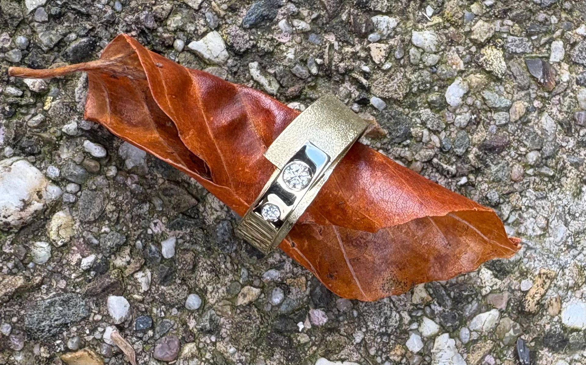 Gouden ring met oranje en witte edelstenen op een groen, met mos bedekt oppervlak.