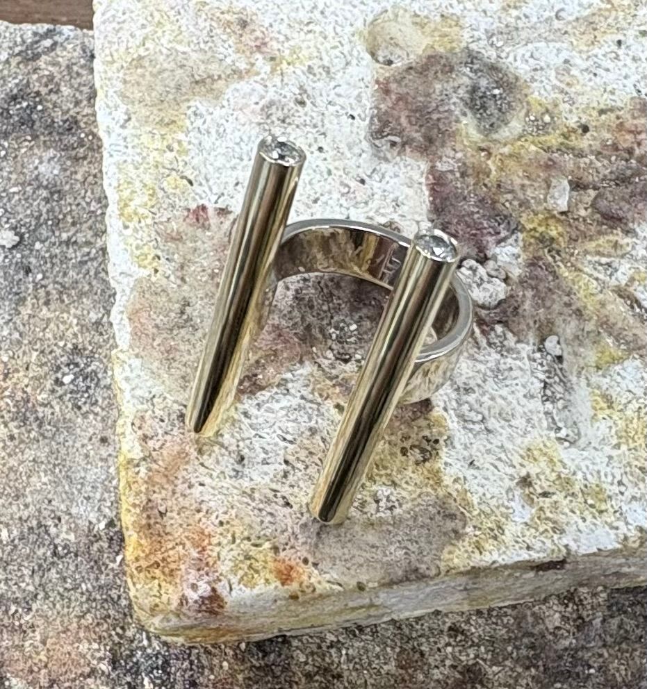 Gouden ring met structuur en een kleine vierkante edelsteen, rustend op een grijs oppervlak.