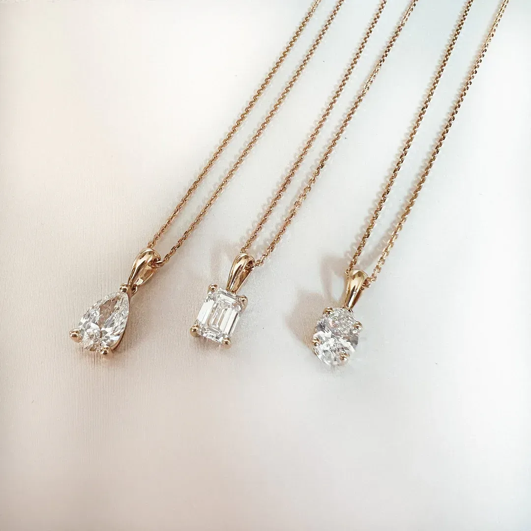 Drie gouden kettingen, elk met een andere diamanthanger: peer-, smaragd- en ovaalgeslepen.