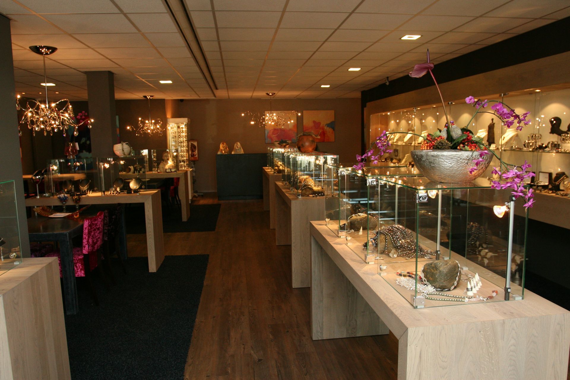 Interieur van een juwelierszaak met vitrines, houten vloer en plafondverlichting.