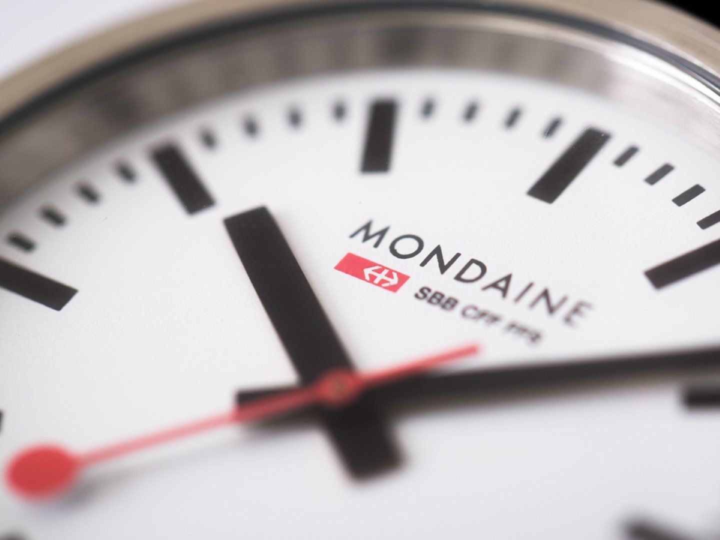Close-up van een Mondaine-horloge, wit met zwarte markeringen en een rode secondewijzer; 