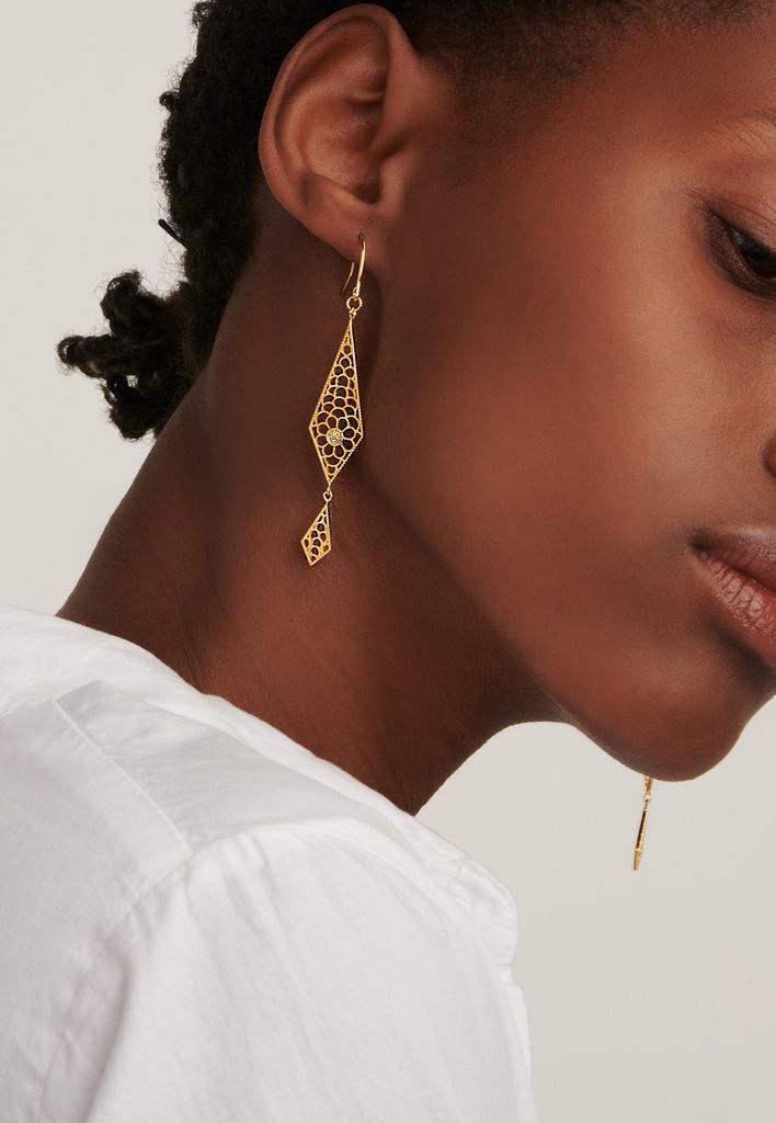 Vrouw met een gouden filigraan oorbel. Ze draagt ​​een wit shirt en haar haar is naar achteren gekamd.