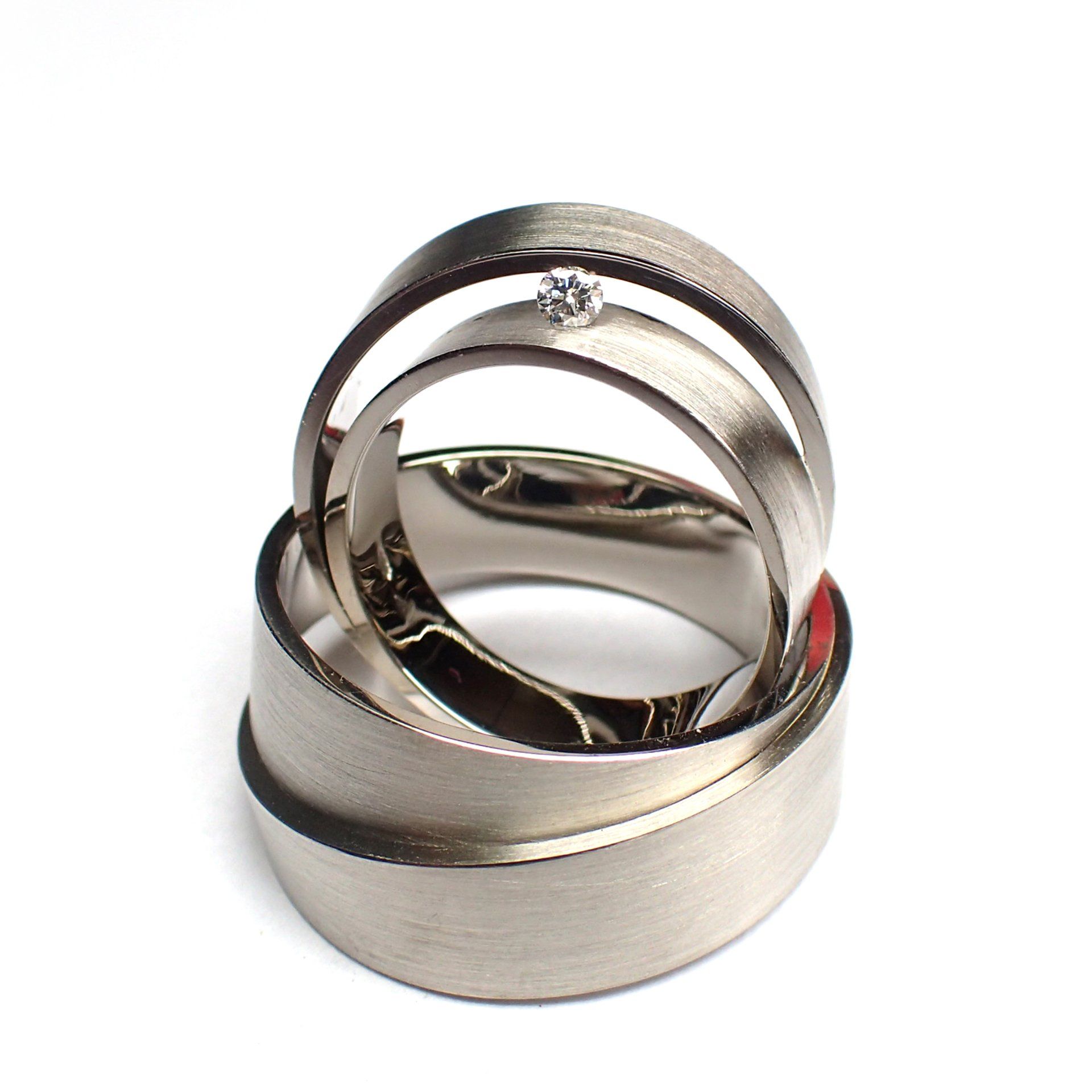 Drie in elkaar grijpende ringen van geborsteld metaal, waarvan één met een klein diamantje.