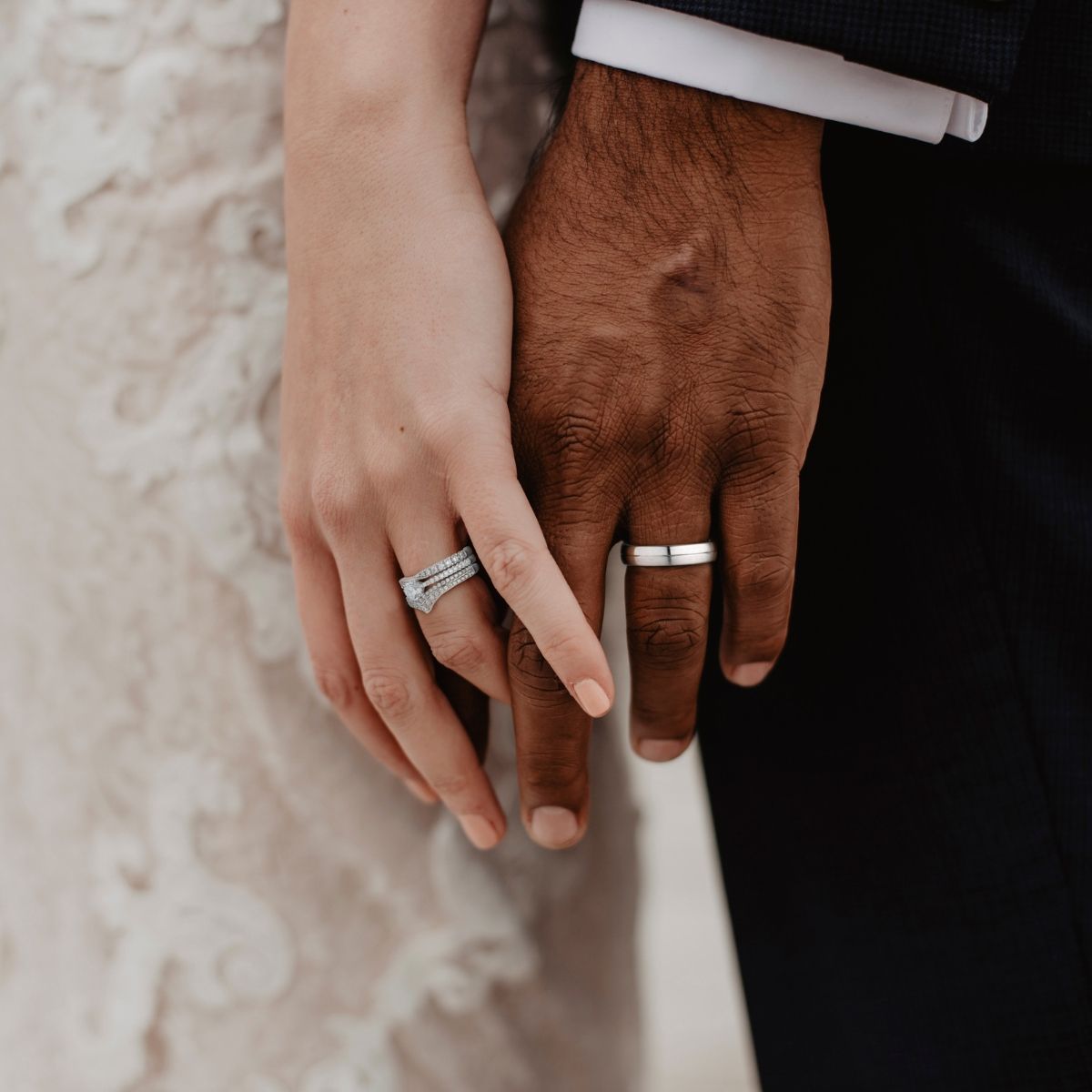 De handen van het echtpaar zijn ineengeslagen, met de trouwringen zichtbaar. De ene hand is licht, de andere donker.