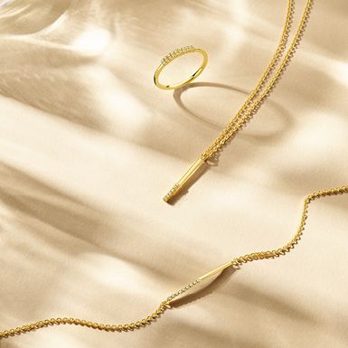 Gouden sieraden op een crèmekleurige achtergrond; ring en twee kettingen.