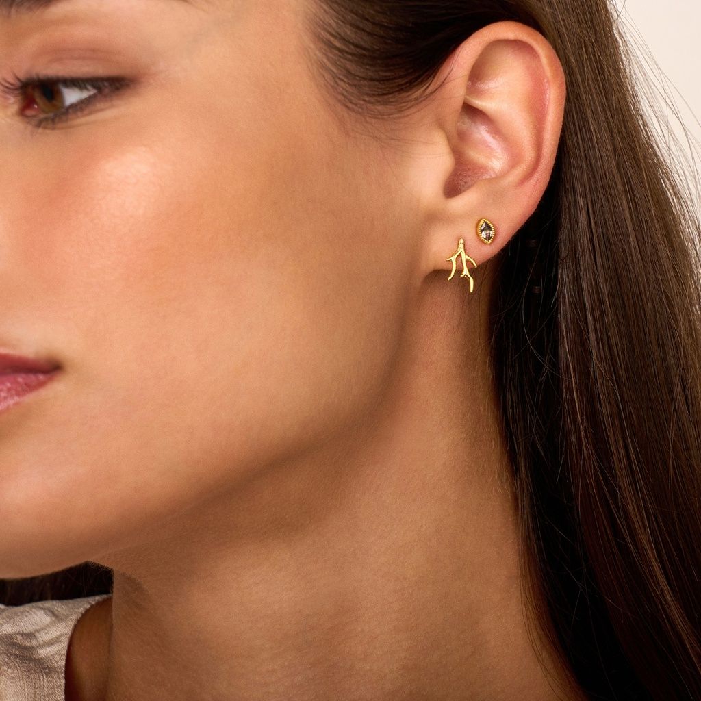 Vrouw draagt ​​gouden oorbellen; één set in de vorm van een mens, de andere bezet met een klein steentje.