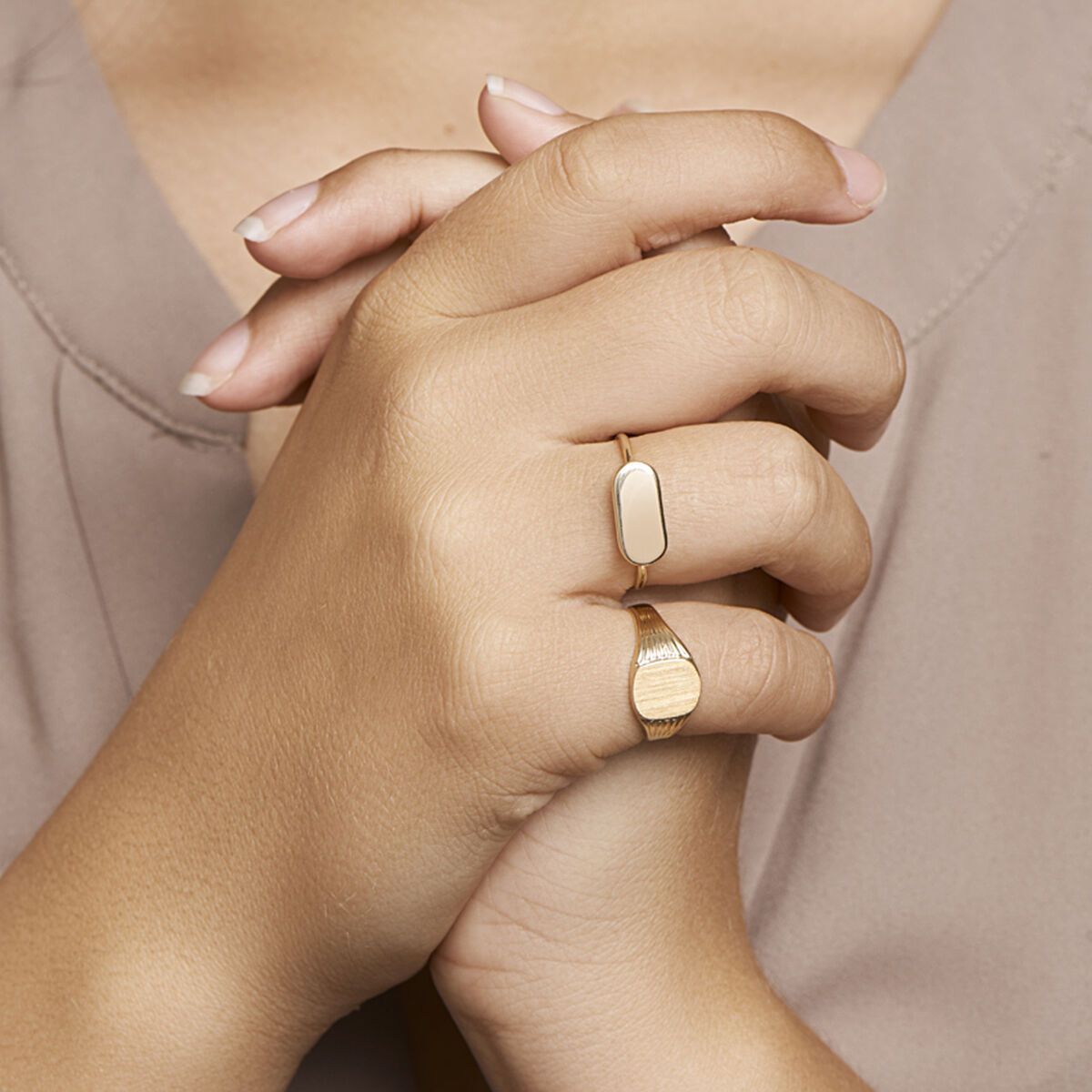 Close-up van handen met twee gouden ringen, waarvan één ovaal van vorm is en de andere een ruw oppervlak heeft.