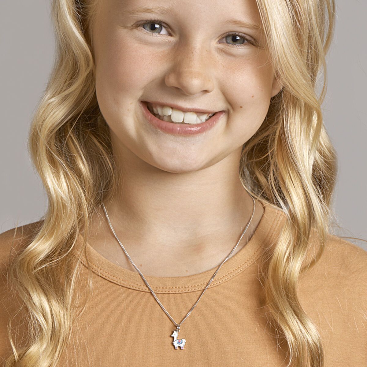 Meisje met blond, krullend haar, lachend, draagt ​​een ketting met een klein hangertje.