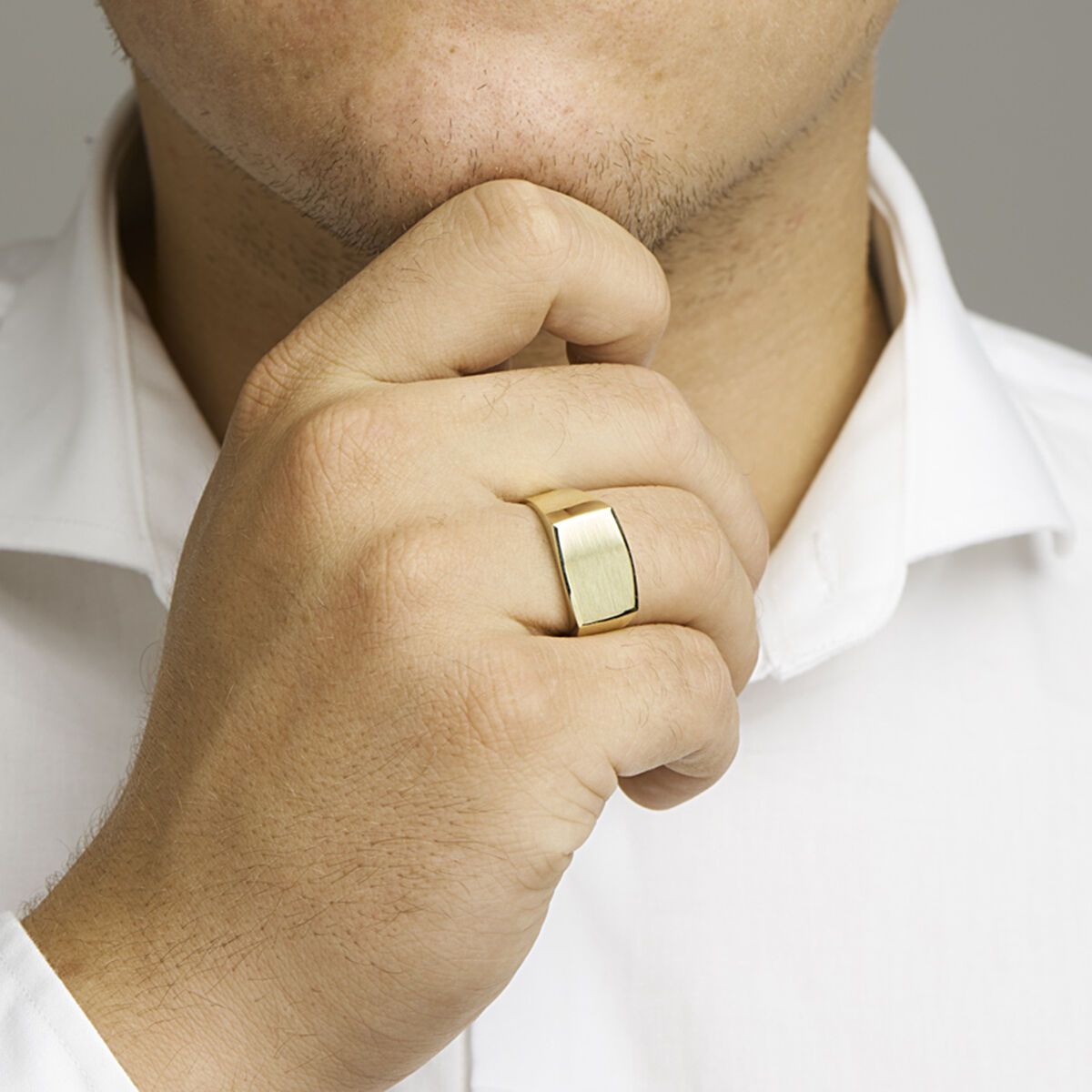 Man met een gouden ring, zijn hand op zijn kin, wit overhemd.