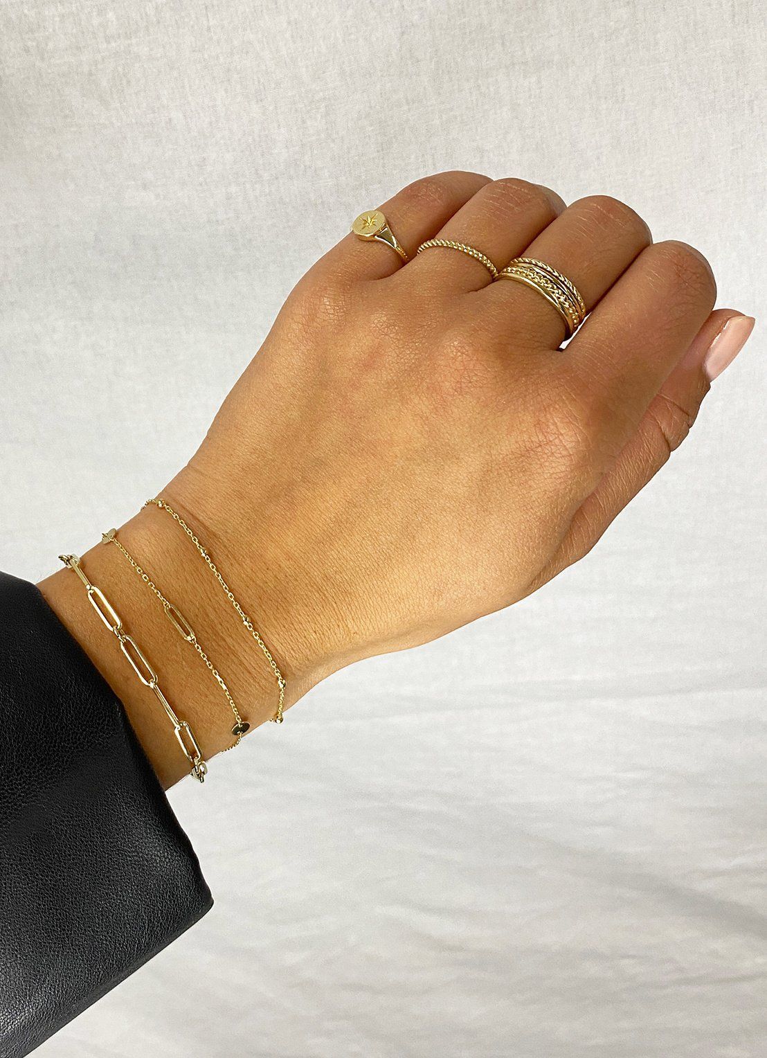 Hand met gouden sieraden: armbanden en ringen. Lichte huidskleur. Tegen een witte achtergrond.