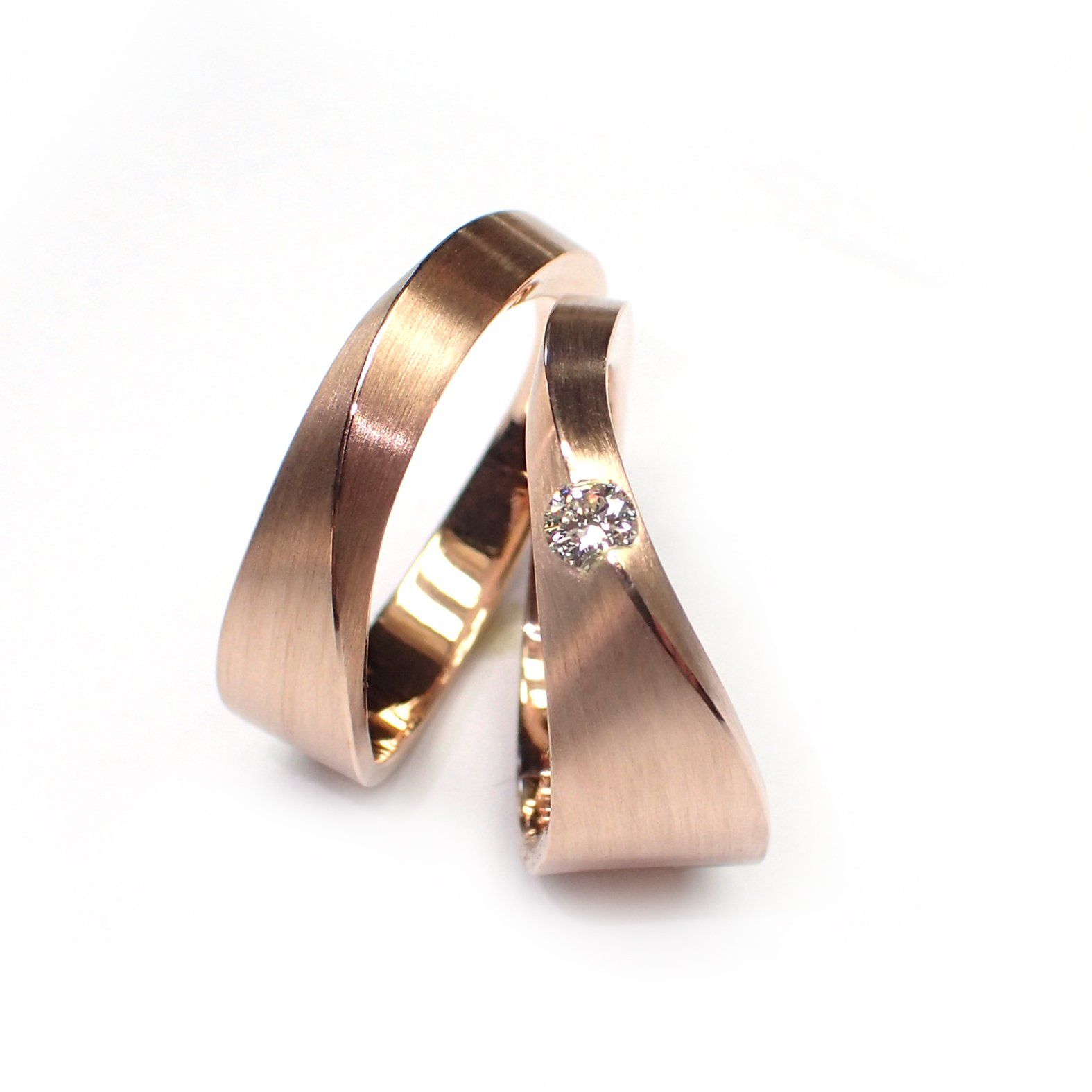 Twee trouwringen van roségoud, waarvan één met een klein diamantcluster.