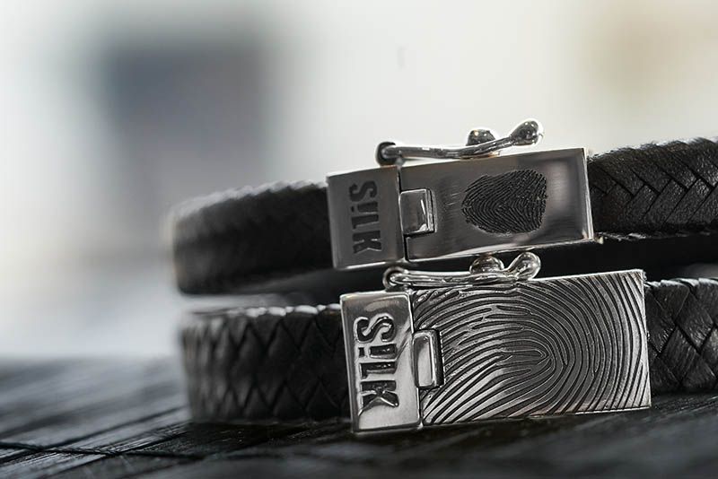 Close-up van twee zwarte leren armbanden met zilveren sluitingen, op beide is een vingerafdruk te zien.