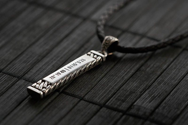 Zilveren hangerketting met een donker structuuroppervlak; gegraveerd met coördinaten.