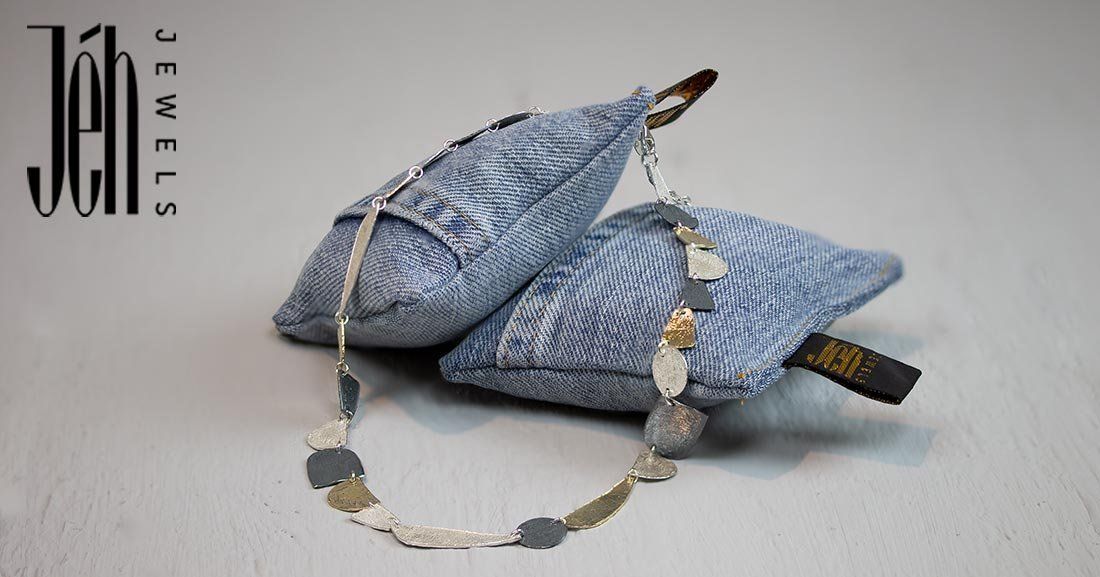 Zilveren en gouden ketting met abstracte hangers op kussens van spijkerstof.