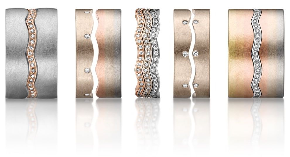 Vijf trouwringen met golvende lijnen van diamanten, verschillende goudtinten en geborstelde metaaltexturen.