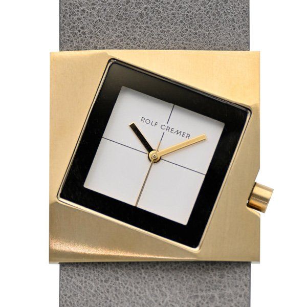 Goudkleurig vierkant polshorloge met een zwart-witte wijzerplaat en grijze band. Op de wijzerplaat staat de opdruk 