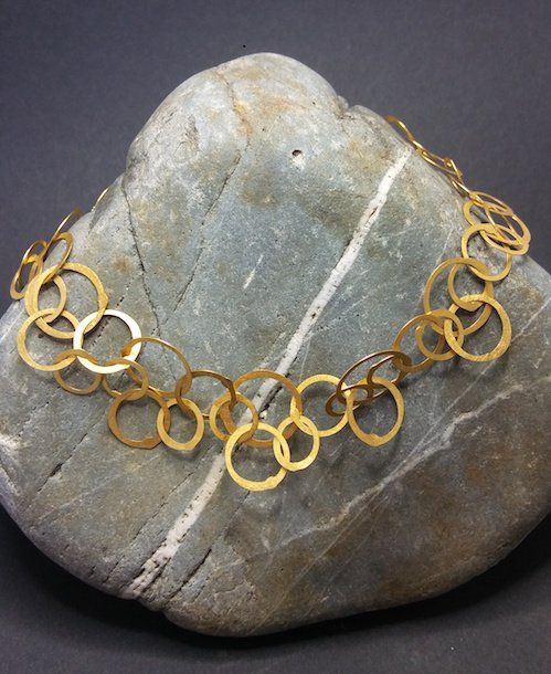 Gouden cirkelketting gedrapeerd over een grijze steen.